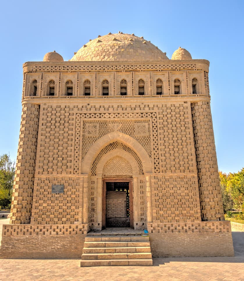 The Samanid Mausoleum: a cube-shaped brick building with a dome, an arched entrance and steps, under a blue sky