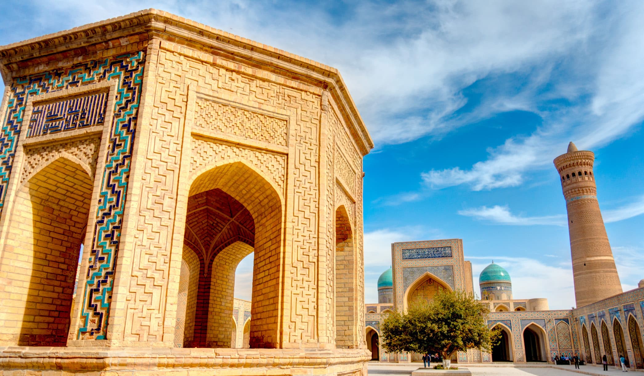 The Poi-Kalyan ensemble: an octagonal brick pavilion with arches and turquoise tilework, with a minaret and blue domes beyond