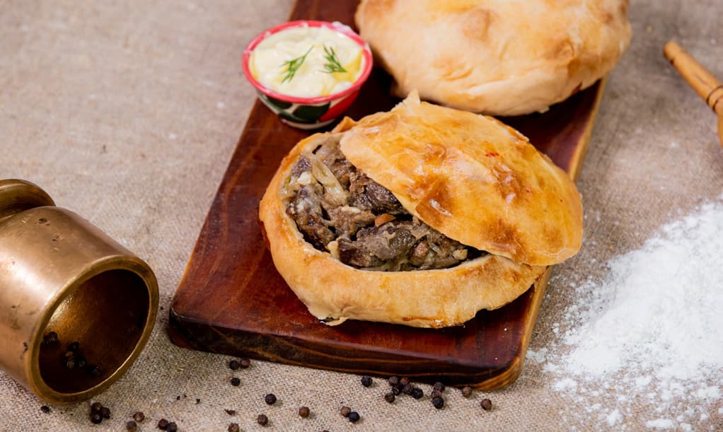 Jizzakh samsa on a wooden board with flour, spices and a small bowl of sauce