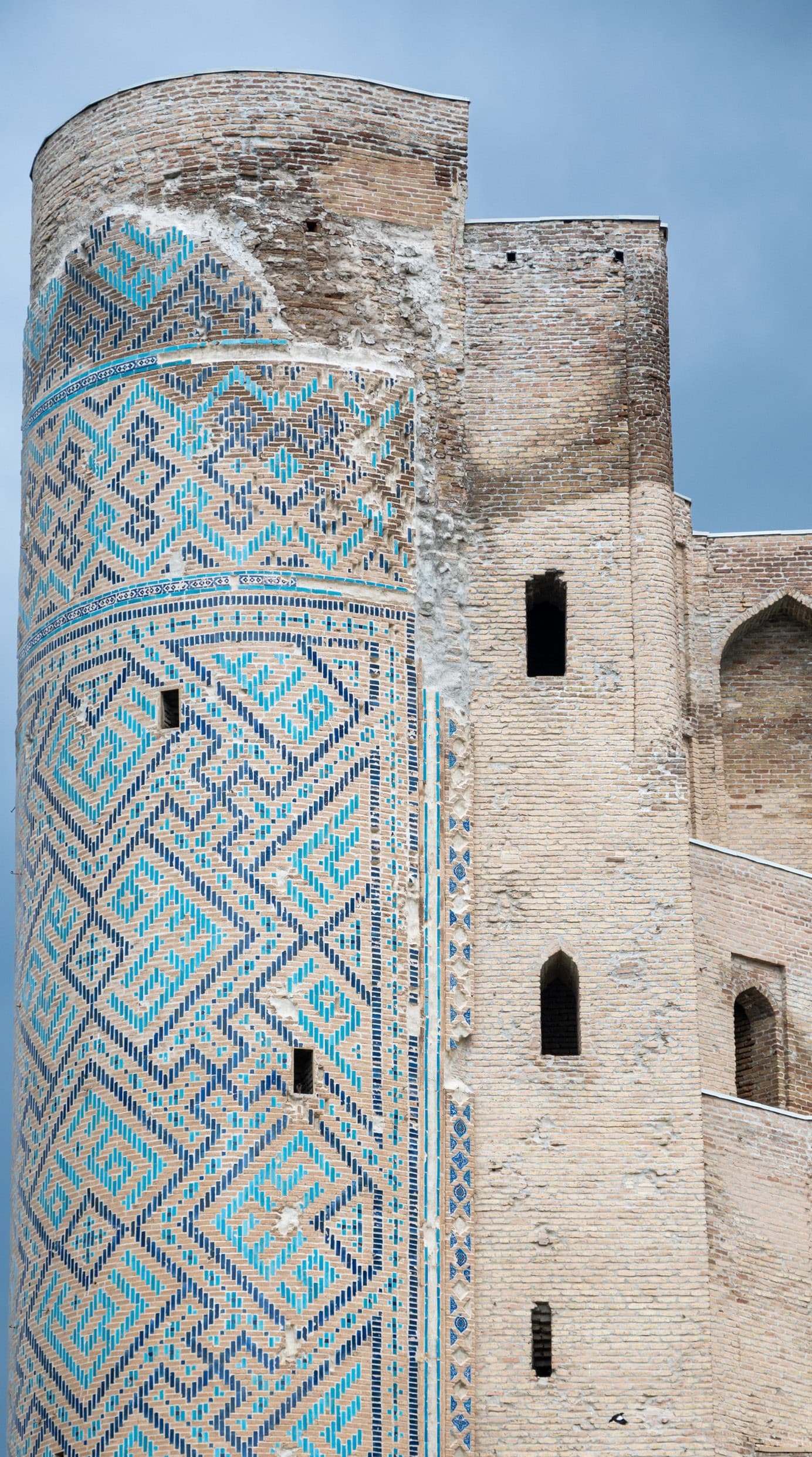 Remains of the Ak-Saray portal in Shakhrisabz: a tall brick pylon faced with blue and white geometric mosaic against a pale sky