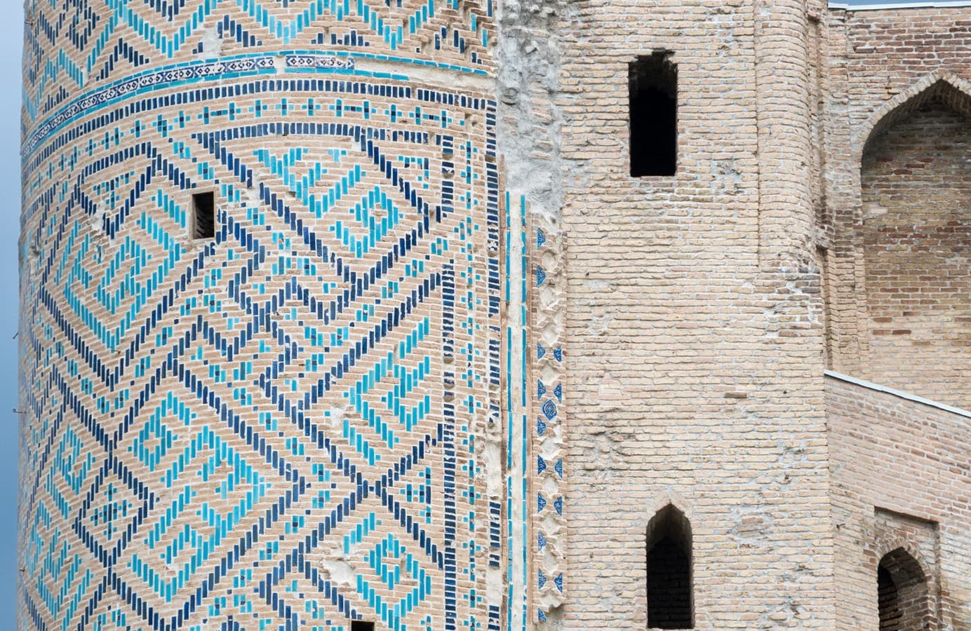 Close view of the Ak-Saray portal remains: a pylon covered in blue and white mosaic beside light brickwork with narrow windows