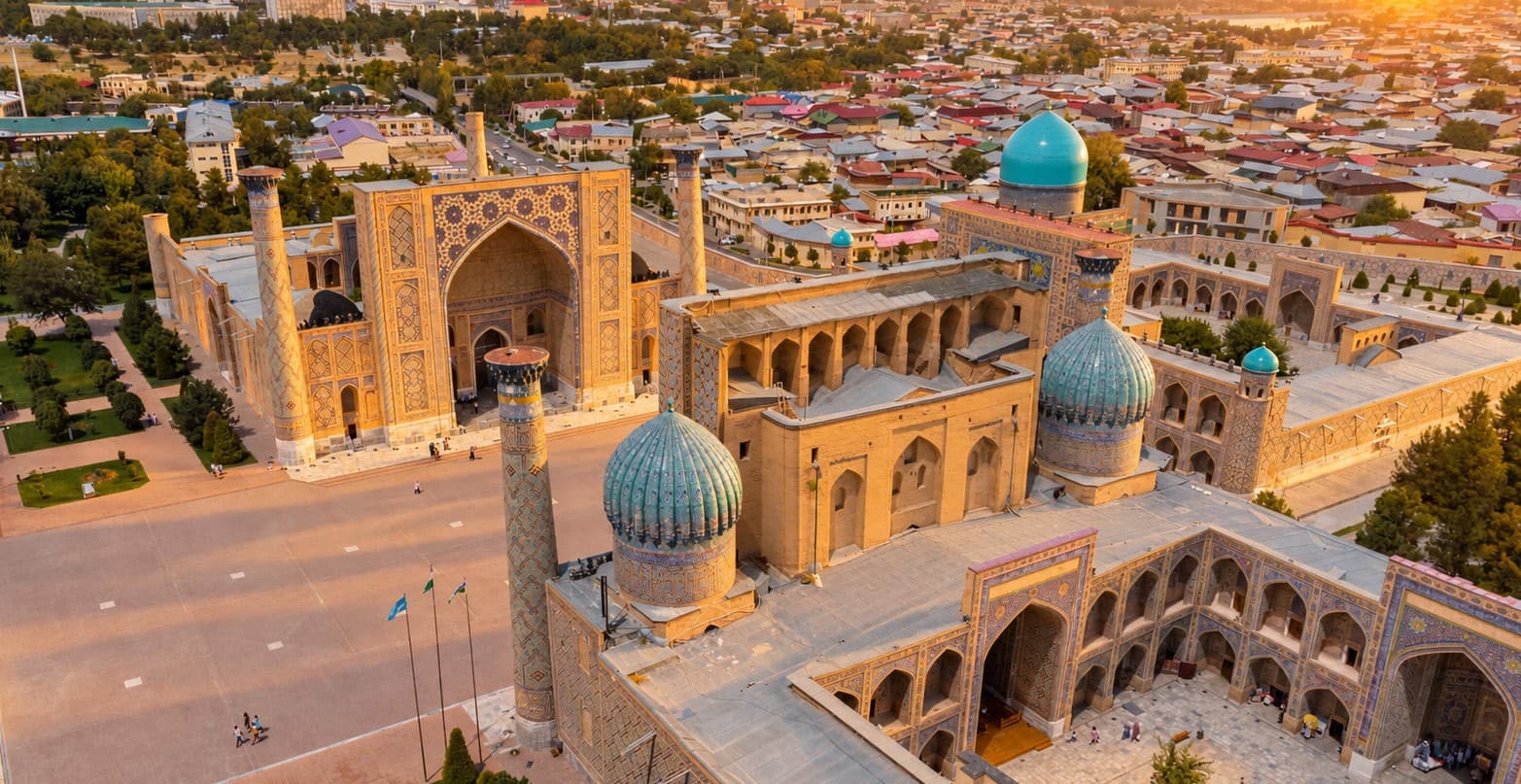 Registan Square in Samarkand seen from above at sunset, with blue domes and the city beyond