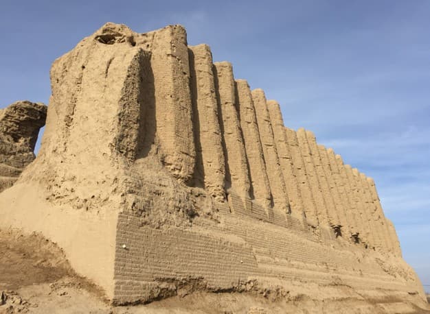 A tall weathered mud-brick wall at Merv with deep vertical ribs, under a blue sky