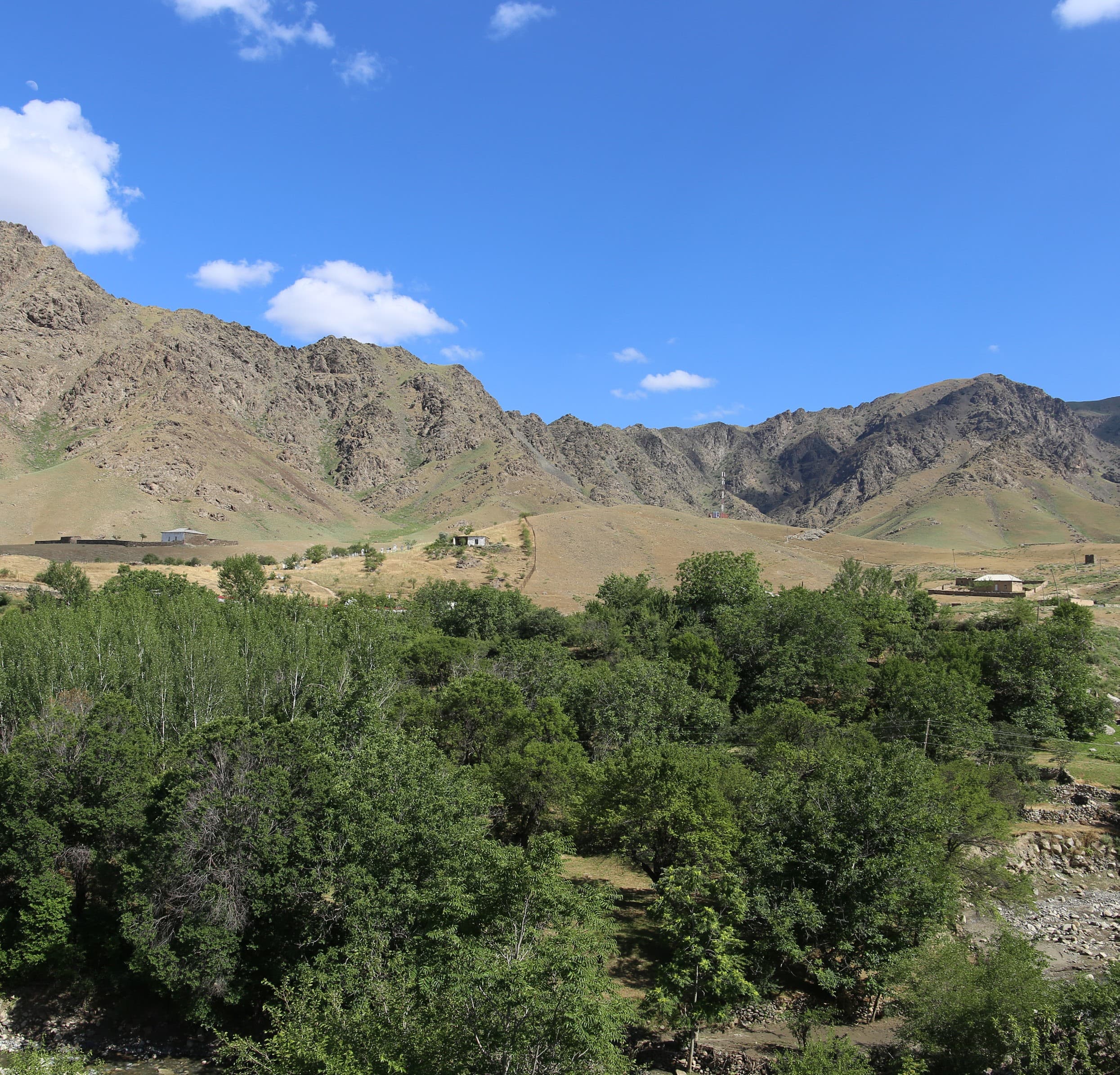 Mountain landscape near Sentob in Nuratau: brown slopes, blue sky with white clouds, green trees and a few village houses below