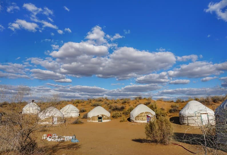 White yurts of a tourist camp on sand under a blue sky with clouds
