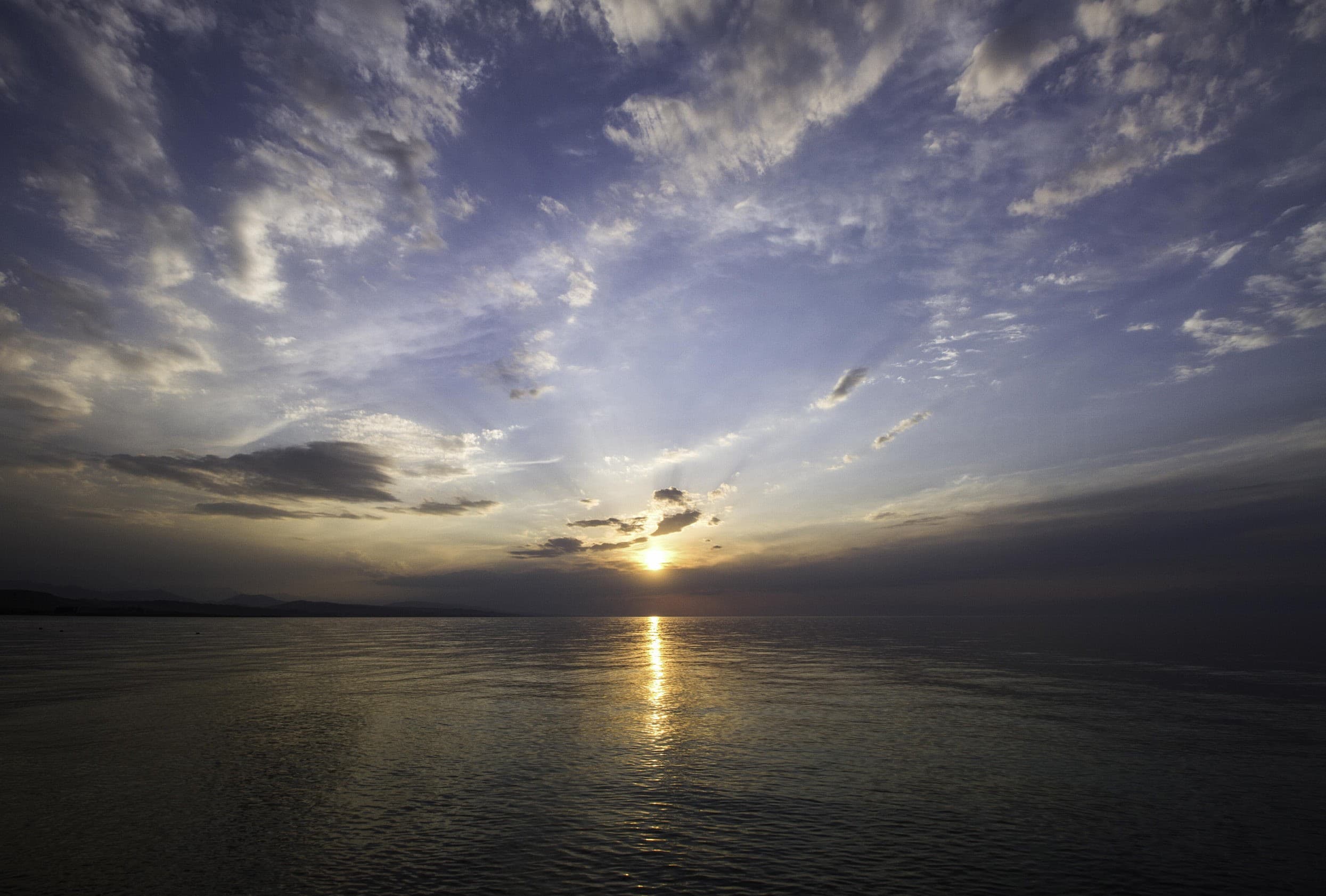 Sunset over Issyk-Kul: a golden path of light on the water beneath a dramatic cloudy sky