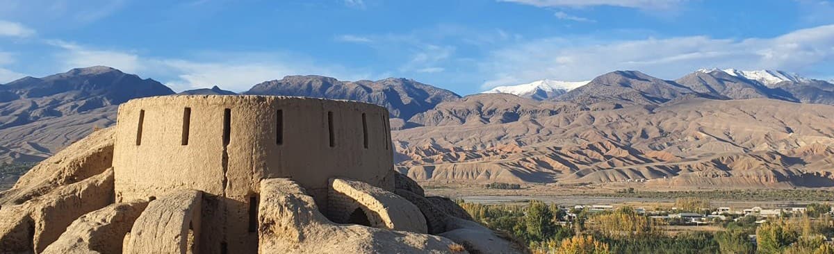 A round clay structure at Ancient Panjakent with dry mountains and snowy peaks behind